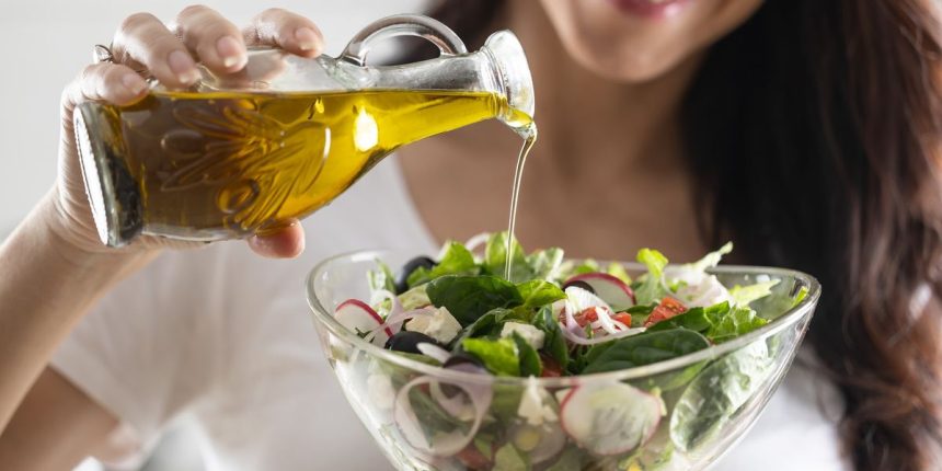 woman pouring olive oil into salad