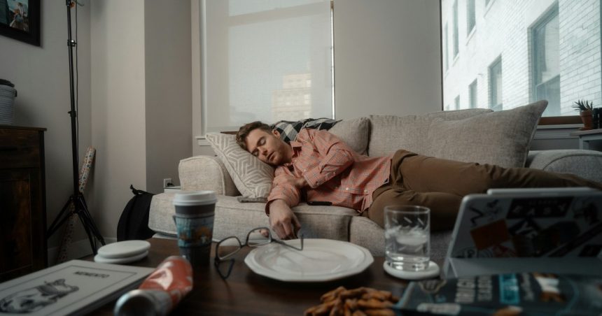 chris lynch man laying on couch sleeping with messy table empty food plates glasses unsplash
