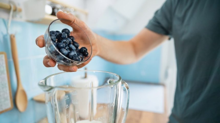 man putting blueberries in blender