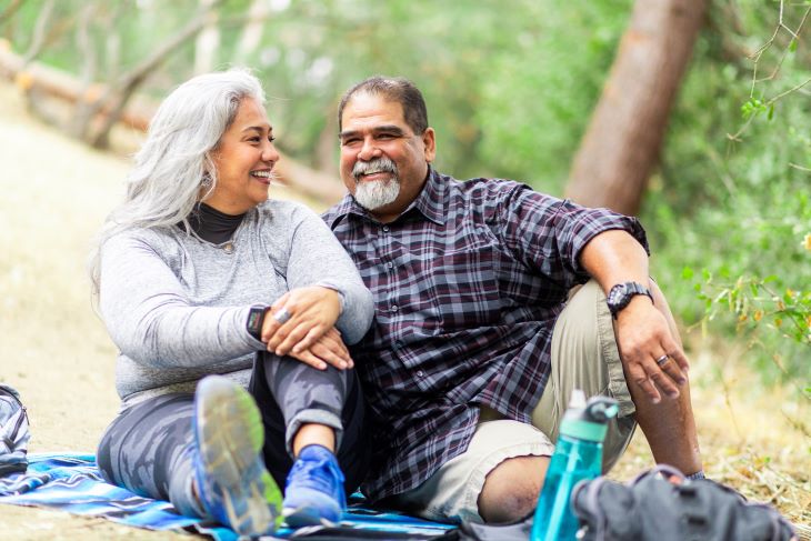 A senior couple enjoying a picnic on a blanket in the woods.